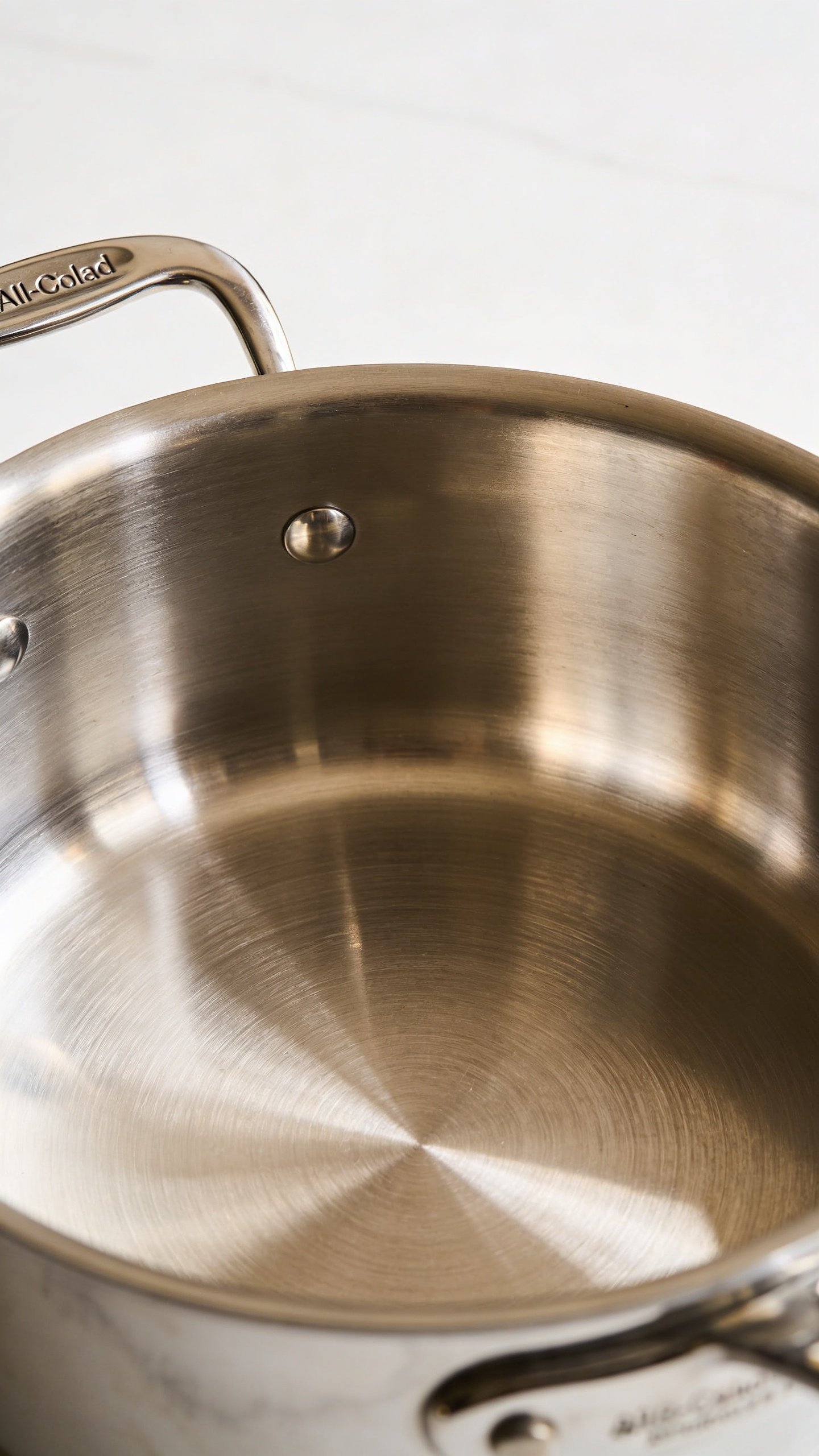 All Clad Vs Calphalon: Sizzle or Simplicity? 2 closeup stainless steel All-Clad pan interior, reflection highlight, brushed finish